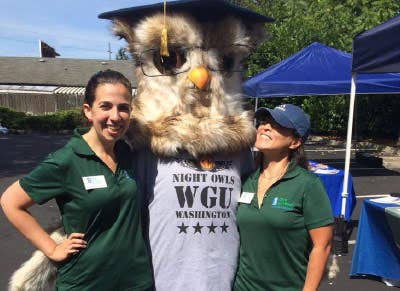 Two volunteers posing with Sage the Owl mascot