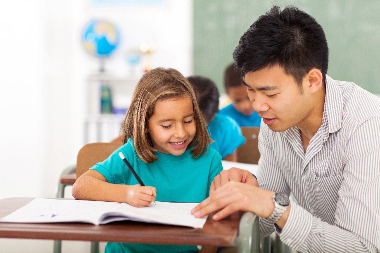 friendly preschool teacher helping little girl with class work