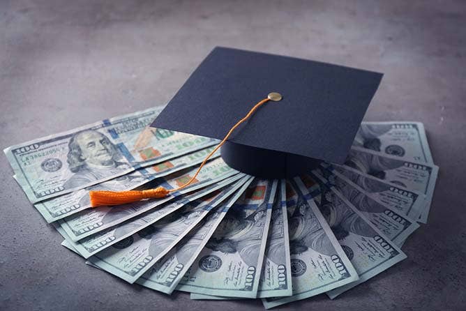 Graduation hat and dollar banknotes on table.
