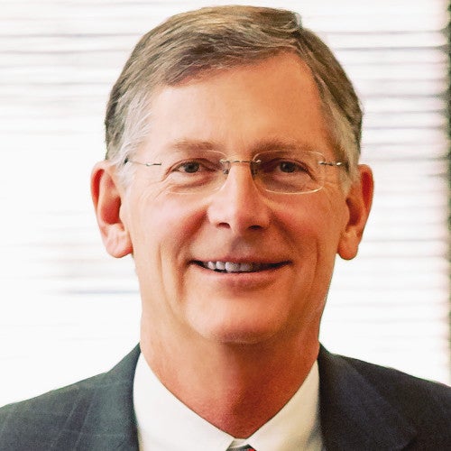 Charles Sorenson is a white man with glasses and grey-brown hair, wearing a suit and glasses against a grey background.
