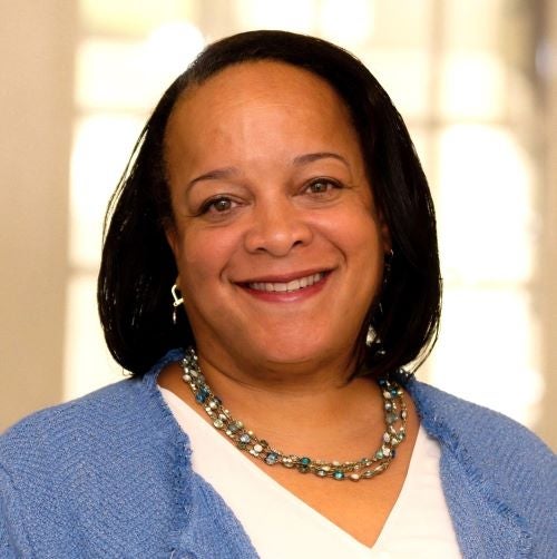Bridget Long is a Black woman with black hair. She is wearing a white shirt with a light blue jacket and a beaded necklace.