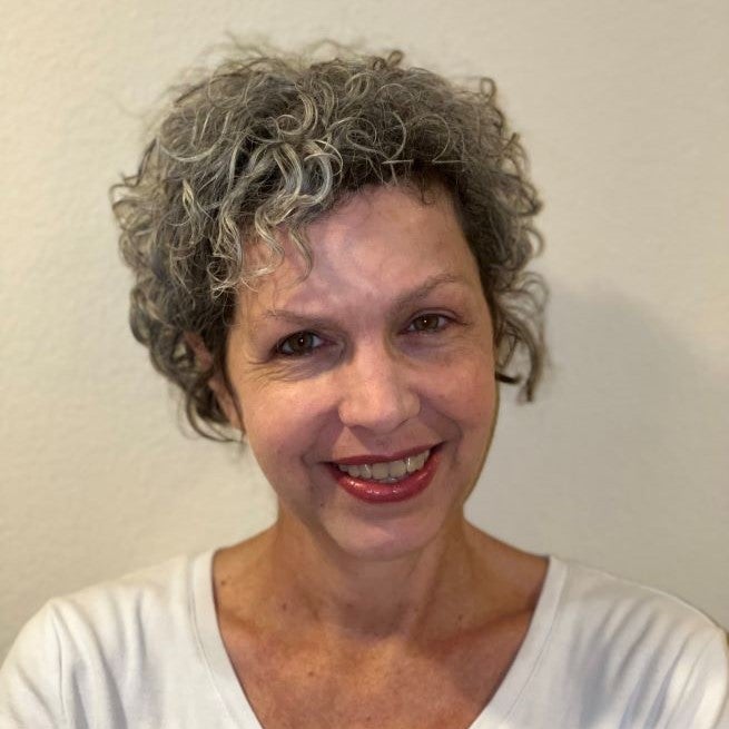 Sandra Sjoberg is a white woman with curly gray-brown hair. She is smiling and wearing a white shirt