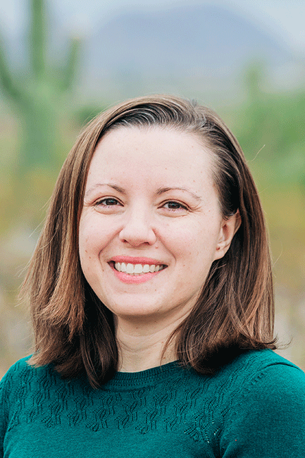 Andrea Burns is a white woman with brown hair standing outside and wearing a green sweater.