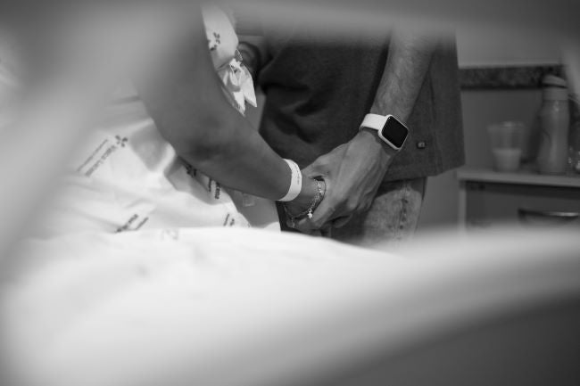 Black and white photo of a hospital patient sitting on a bed with a person holding their hand.