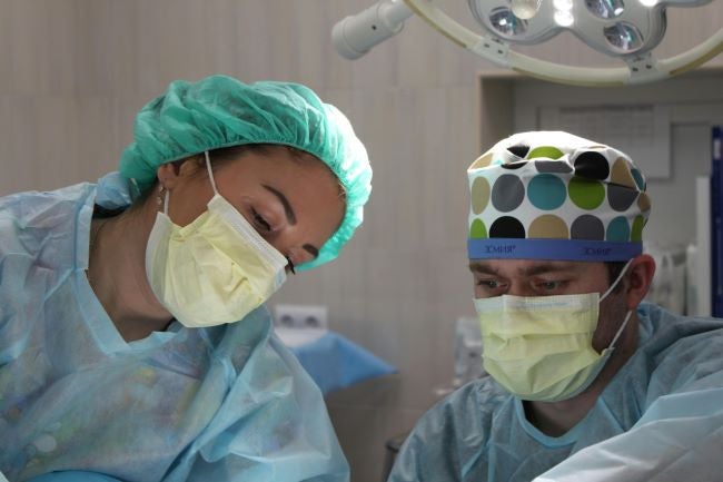 Two health professionals with masks and gowns work together in an operating room