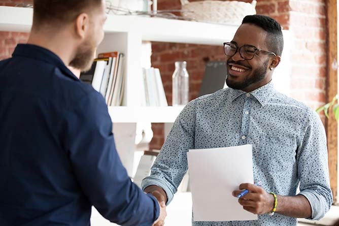 Mixed race executive company ceo shaking hands with client during business negotiations meeting in office. African american recruiter greeting handshaking with vacancy candidate before job interview