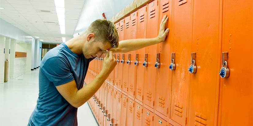 A student rubs the bridge of his nose whilst leaning against a locker.