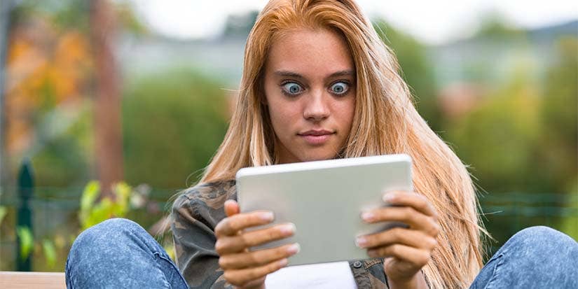 A girls looks at a tablet with a shocked expression.