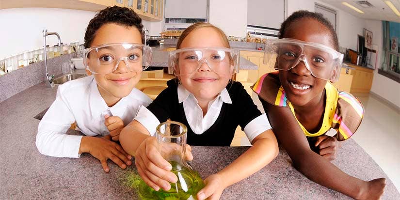 Three young students wearing safety glasses smile in the camera.