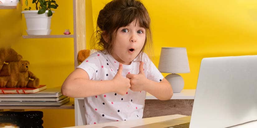 A young girl gives two thumbs up against a yellow background.