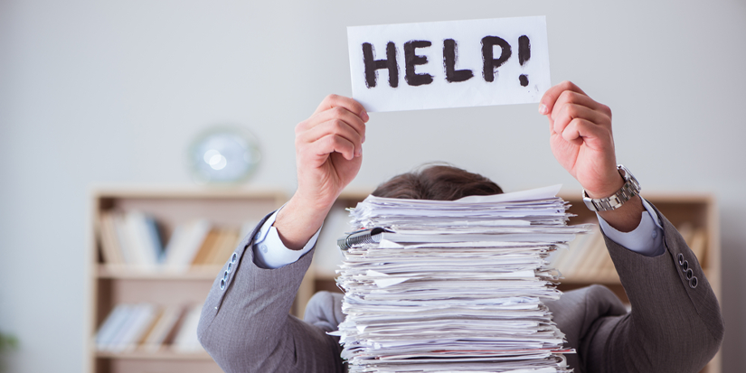 Teacher overwhelmed with paperwork holding a help sign 