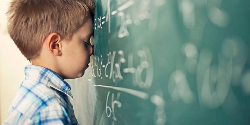 A disappointed students leans against a chalkboard using his forehead.