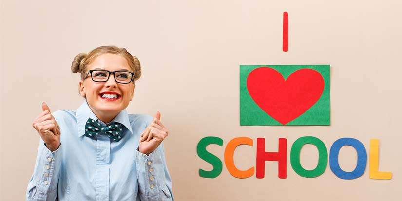 A young girl wearing glasses and a bowtie sits excitedly by a sign that says, "I love school."