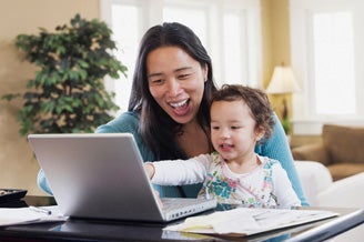 Mom and baby sitting at computer laughing.