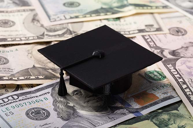 A graduation cap sitting atop dollar bills.
