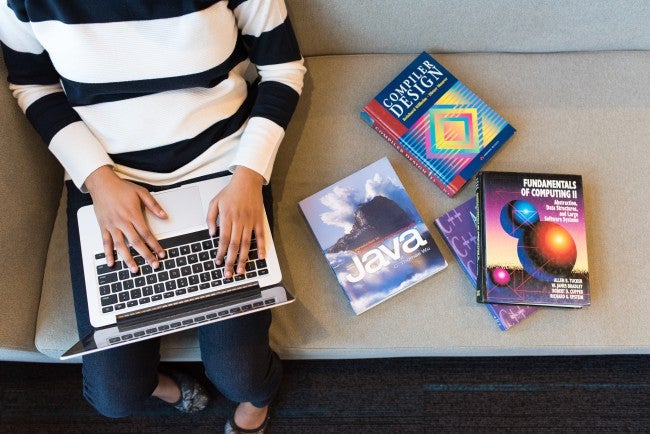 Hands on computer keyboard, next to computer coding books