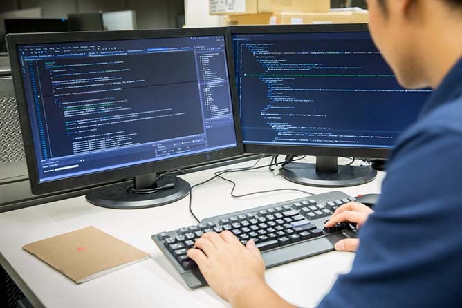 Male programmer works at a dual monitor desktop.