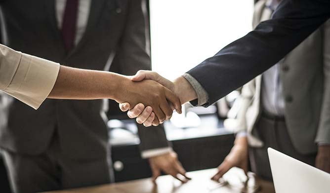 Two business people shake hands over a conference table.