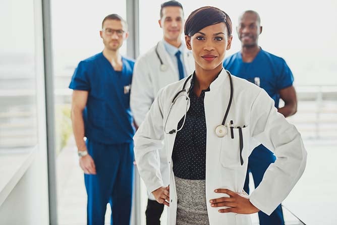 A nurse leader stands prominently with hands on her hips in front of a group of nurses.