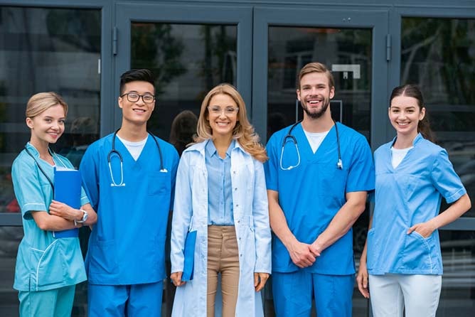 Five healthcare professionals pose, smiling in front of hospital doors.