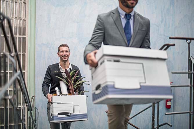 Two businessmen climb stairs while carrying a box of their belongings.