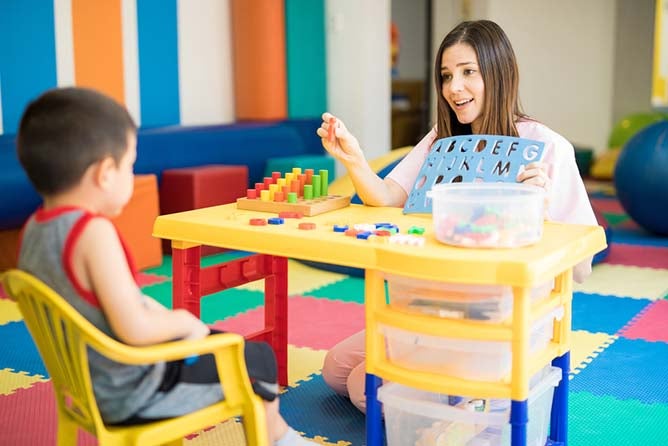 A language therapist works in a special education classroom with a young student.