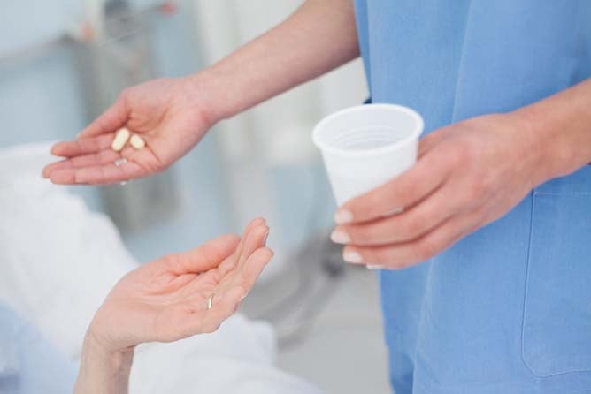 A nurse holds some pills in one hand and a cup of water in the other.