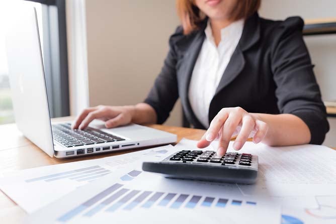 An accountant types into a 9-key with graphs and charts strewn about her desk.