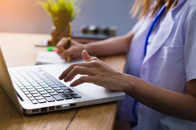 A doctor types on a laptop in search of medical or patient information.
