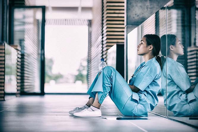 Side view of nurse sitting on floor in hospital corridor.