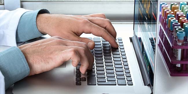 Health information management employee typing on computer next to stethoscope and patient files