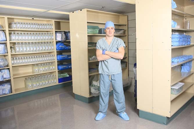 A medical professional folds his arms among shelves with various medical records and items throughout.