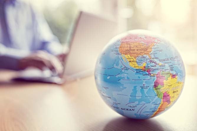 A globe sits in the foreground while a man works on a laptop in the background.