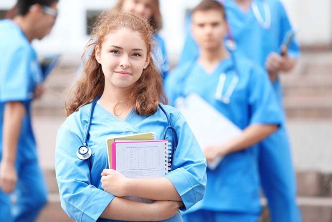 A young nurse holds a stack of books in front of her colleagues.