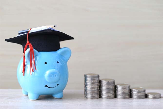 multiple stacks of coins and one blue piggy bank with graduation cap