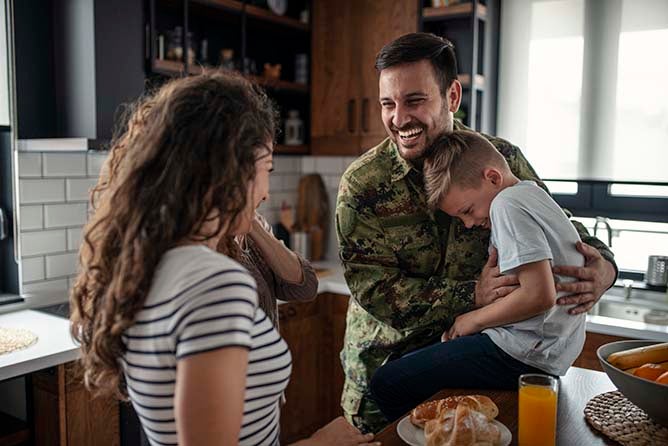 An American soldier excitedly plays with his family in their kitchen.