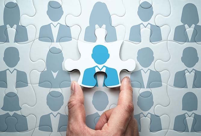 A hand places the final piece of a puzzle completing an image containing various icons representing people.