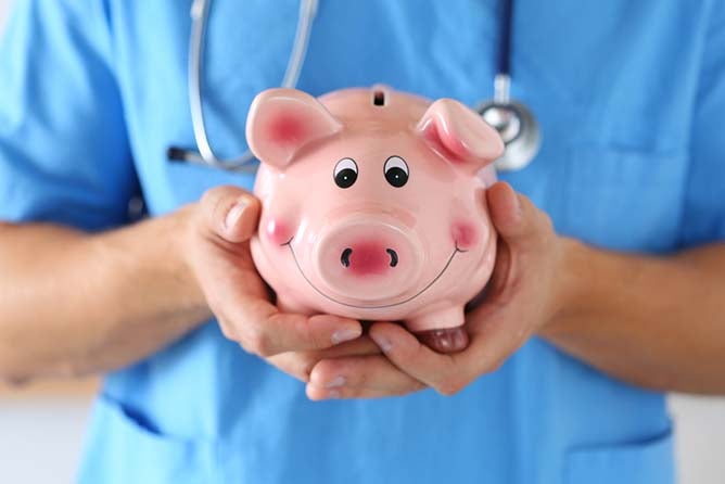 A person in scrubs holds a piggy bank in both hands.