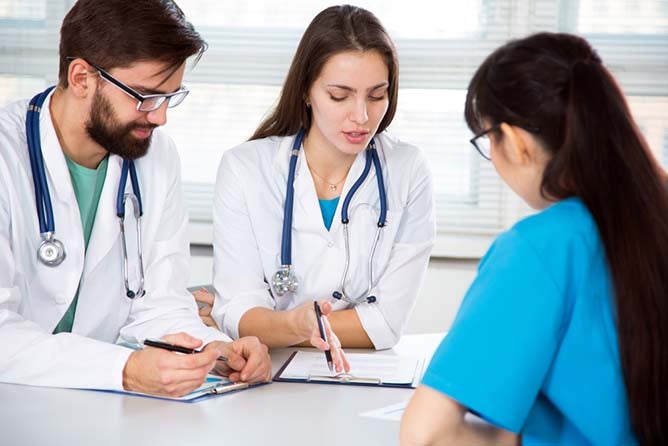 A couple doctors and a nurse sit together in a meeting.