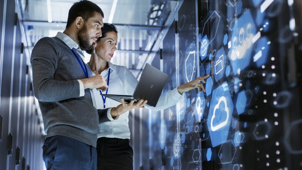 Two IT professional look at server racks overlaid with digital icons.
