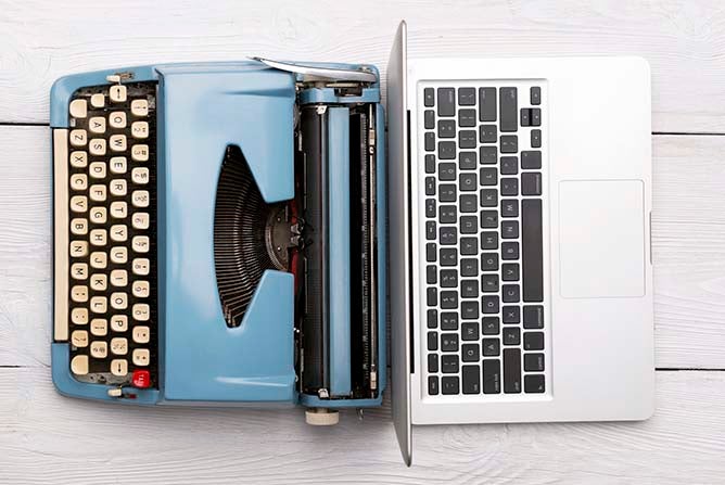A modern laptop sits next to a retro typewriter.