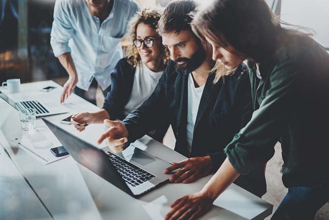 A group of IT professionals look at a laptop screen.