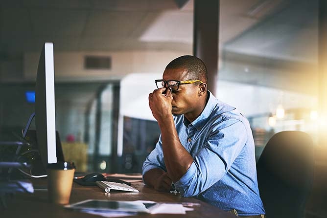 A man working on a computer rubs the bridge of his nose.