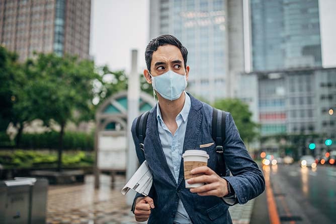A businessman walks down a city street wearing a mask.