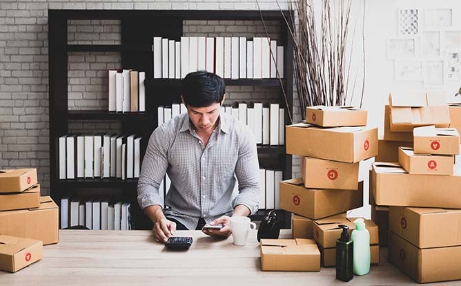 A man surrounded by boxes completes a transaction on his phone.