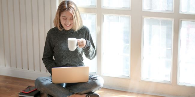 Woman sitting on floor with laptop holding cup of coffee