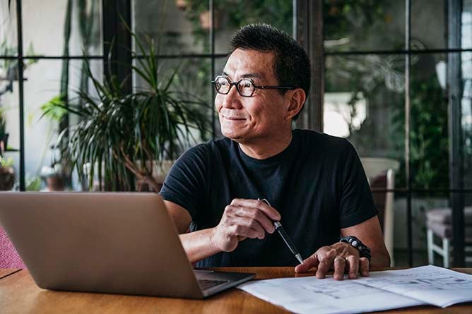 A cheerful man sits at his desk while calmly looking out the window.