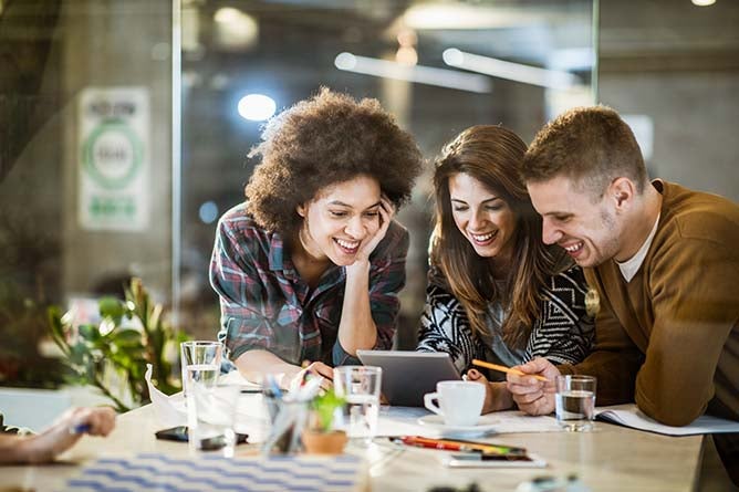 A group of young people gather around a table to look at a tablet.
