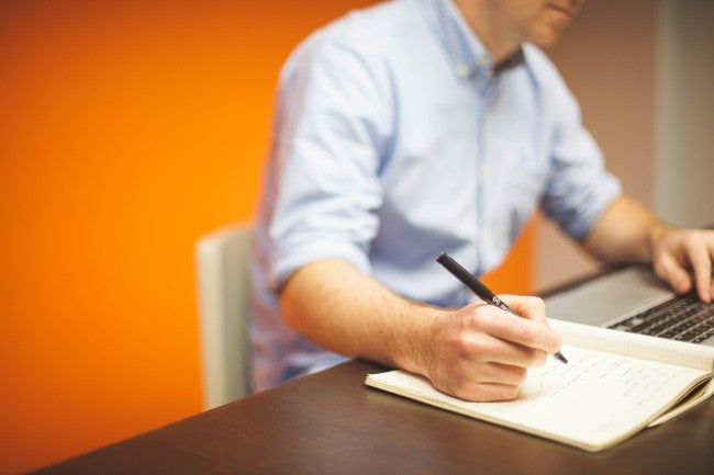 Man writing on notebook at computer