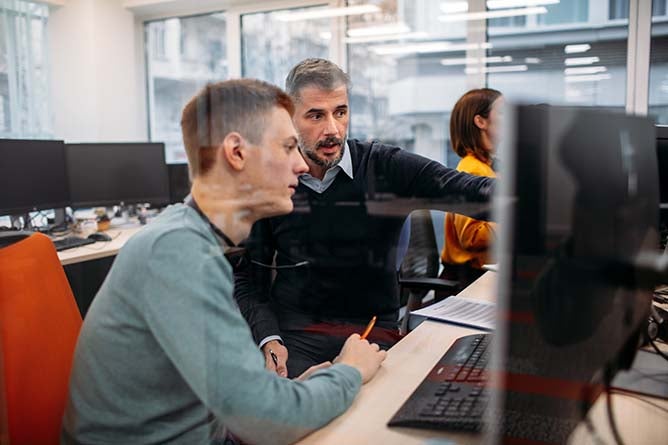 Two IT professionals examine one of the worker's work.